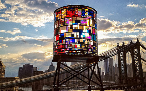 A city rooftop with a stained-glass tower beside luxury designer rugs at sunset.