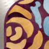 Close-up of a luxury designer rug with abstract yellow, purple, and blue shapes.