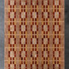 Luxury custom designer rug in geometric plaid, red-orange-beige, on dark floor.