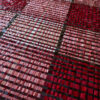Close-up of a luxury designer rug in woven red, pink, and burgundy plaid pattern.