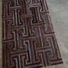 Luxury designer rug with geometric maze pattern in brown and gray on concrete floor.