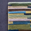 A close-up of Custom 02666 luxury designer rug, handmade wool with multicolored stripes on a dark gray floor.