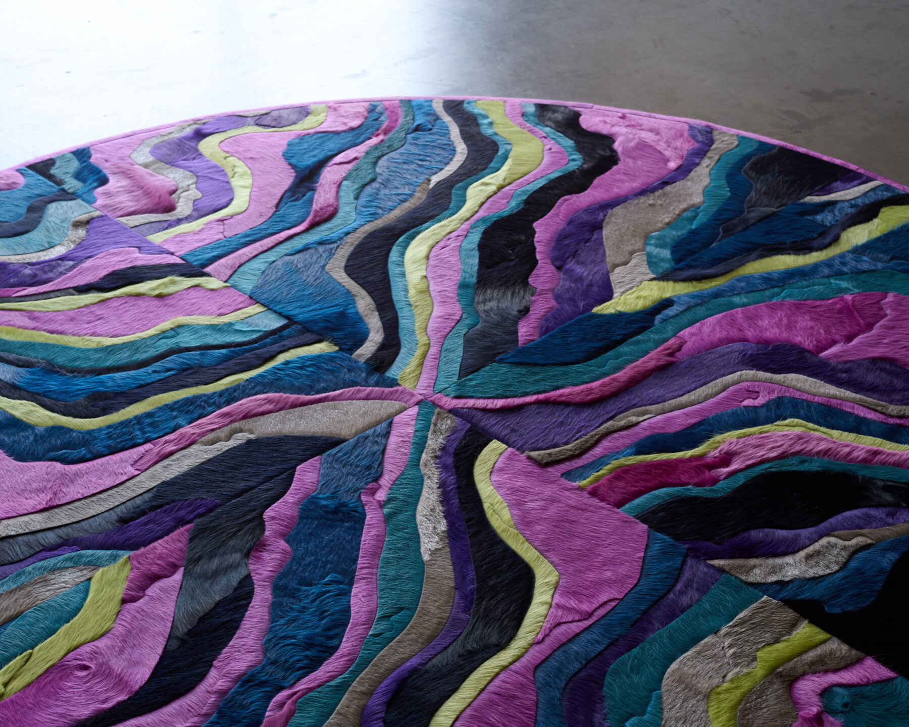 The Submerge 02842 luxury designer round rug features wavy stripes in vibrant hues on a concrete floor.