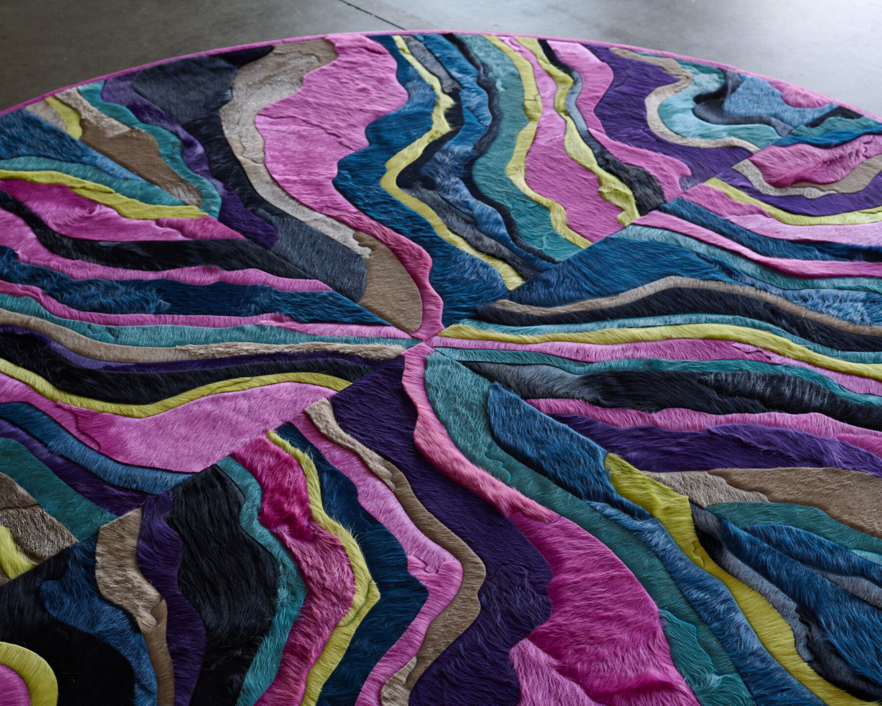 This luxury designer rug features a round, multicolored motif with wavy, radiant stripes.