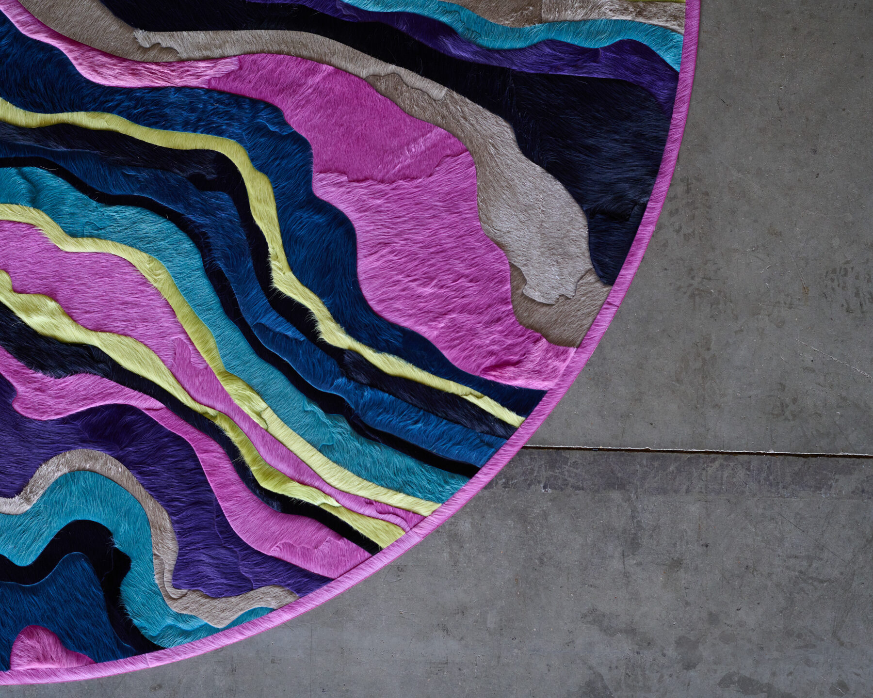 Submerge 02842 luxury designer rug features abstract, wavy patterns in pink, blue, yellow, and beige on a concrete floor.