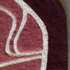 Close-up of luxury designer rug Custom 02633 with abstract pink, maroon, and cream curves on concrete floor.
