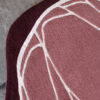 Close-up of a luxury custom designer rug with abstract maroon, pink, and cream lines on concrete.
