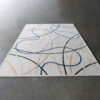 Luxury designer wool rug in beige, with abstract blue, black, and brown lines on a gray floor.