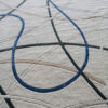 Luxury designer wool rug in beige with curved blue, brown, and gray lines, abstract high-end pattern.