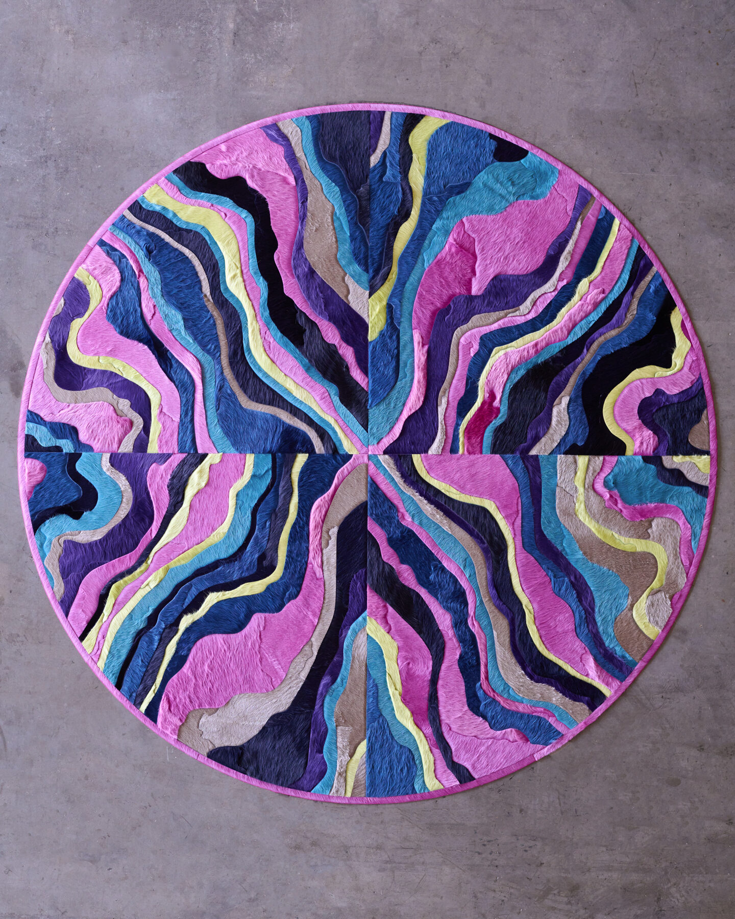 Submerge 02842 is a luxury designer circular wool rug with wavy layered colors on a concrete floor.