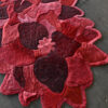 Close-up of a luxury custom designer rug with red and burgundy floral patchwork on gray tile.