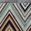 Luxury designer rug with a teal, cream, and gold chevron pattern on concrete floor.