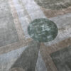 Close-up of a luxury designer rug, Atlas 03143, featuring handmade wool geometric patterns in muted green, gray, and beige.