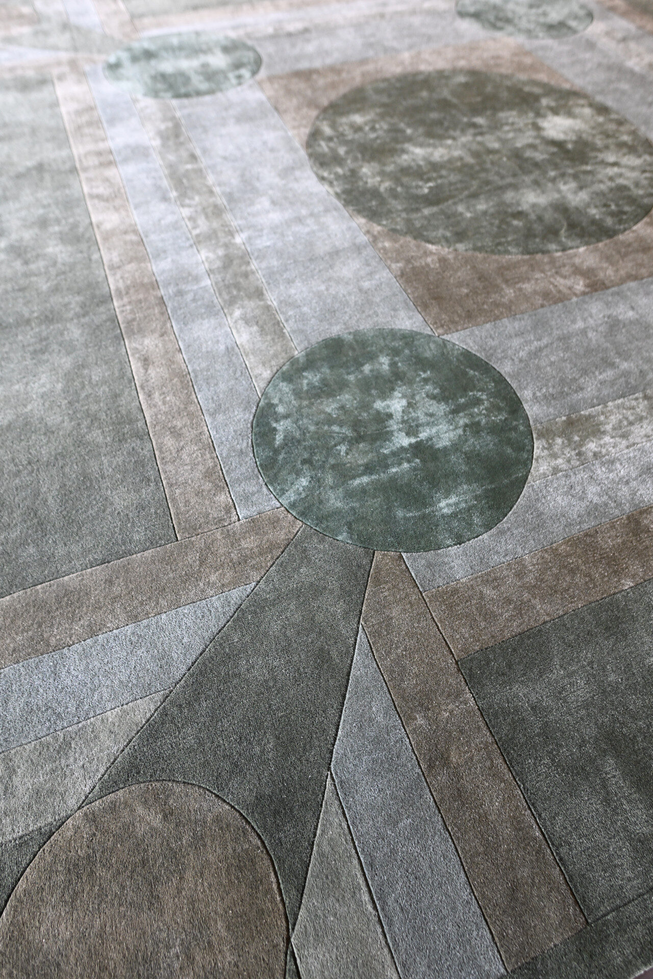 Close-up of a luxury designer rug, Atlas 03143, featuring handmade wool geometric patterns in muted green, gray, and beige.