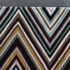 Close-up of Custom 03524 luxury designer rug, featuring a geometric chevron pattern in gold, teal, maroon, and cream on a dark floor.