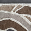 Close-up of Bloom 03448 luxury designer rug with abstract wavy pattern in brown and cream on a gray floor.