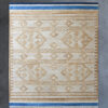 Luxury custom designer rug with a beige geometric pattern and blue-striped edges on a gray floor.
