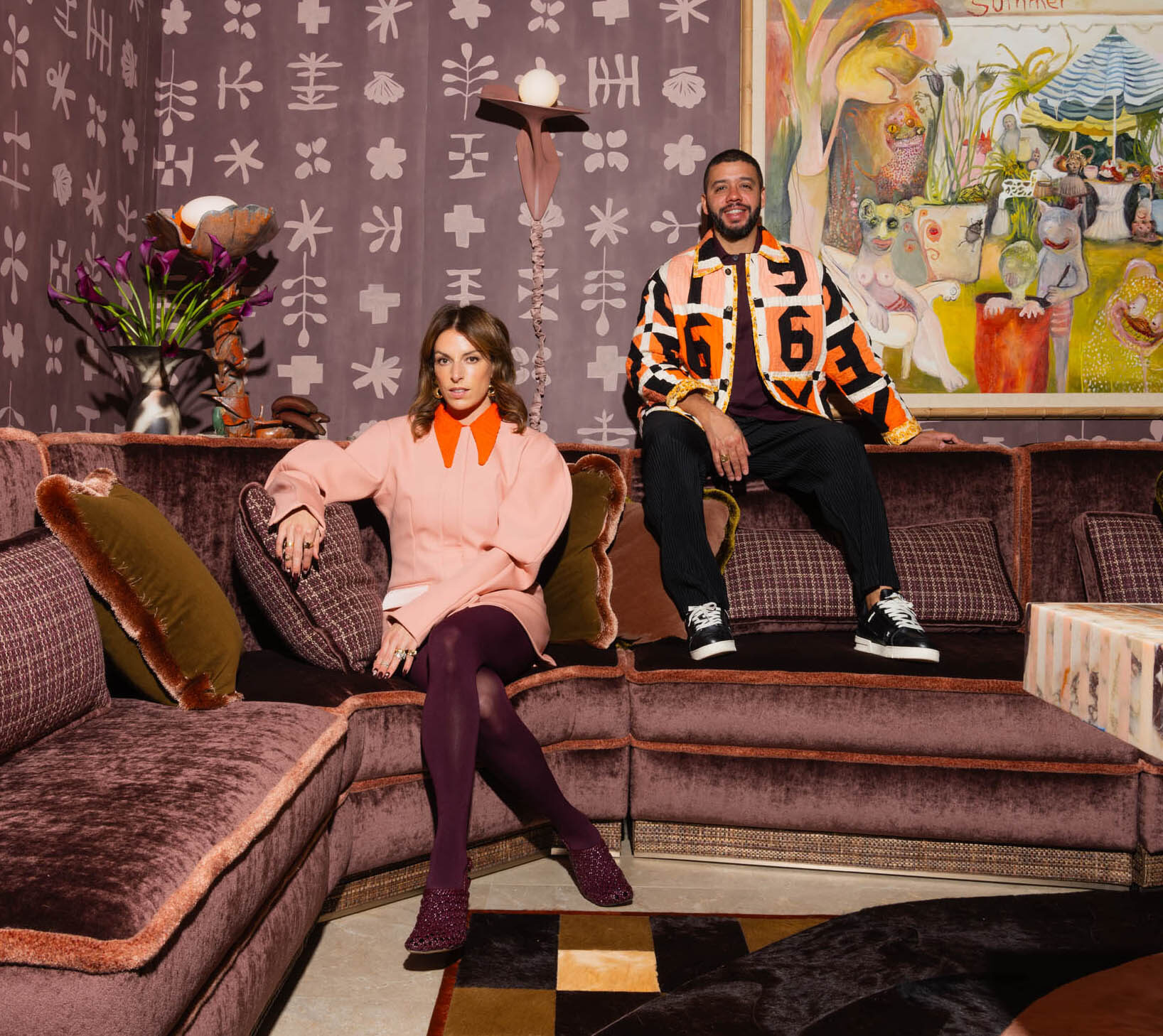 Two people sit on a purple sofa over a luxury designer rug in a patterned, art-filled room.