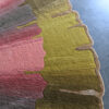 Close-up of Custom 26496, a luxury designer rug with pink, green, and brown gradients on concrete.