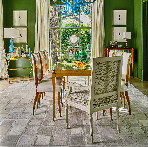A dining room with green walls and a luxury designer rug beneath a wooden table.