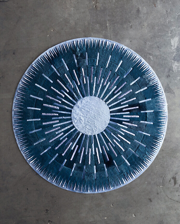 Luxury designer round rug with a blue and white radial pattern on concrete flooring.