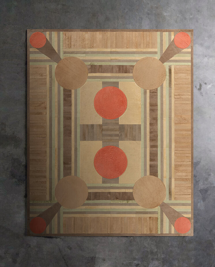 Luxury designer rug with geometric tan, beige, and orange shapes on gray concrete floor.
