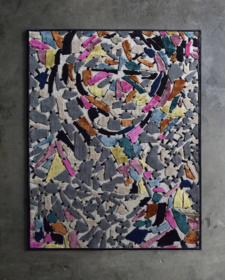 A luxury designer rug with colorful abstract patches hangs on a concrete wall, exemplifying high-end handmade wool rugs.