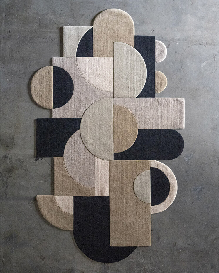 Luxury designer rug featuring overlapping geometric shapes in neutral and dark tones on a concrete floor.