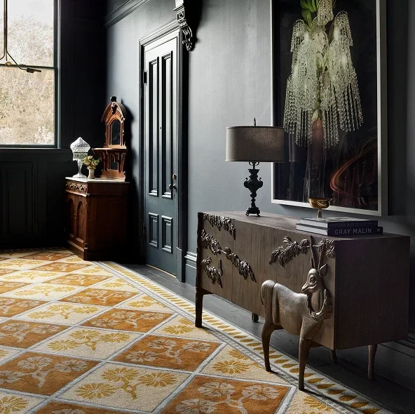 A hallway with dark walls and decorative furniture showcases a luxury designer rug in yellow and white beneath a sideboard with art.