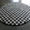 A round luxury designer rug with a black, white, and gray houndstooth pattern on concrete.