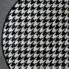 Luxury designer Blackdog Hide 14697 round rug with black and white houndstooth pattern on a grey floor.