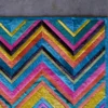 Close-up of a luxury designer rug, handmade with vibrant chevron stripes, on gray flooring.
