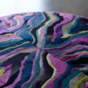 Luxury designer round rug, handmade hide with wavy purple, blue, green layers on polished floor.