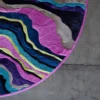 The Submerge Hide 14897 is a luxury designer round rug with wavy multicolored patterns blending into a gray floor.