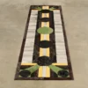Luxury designer rug with geometric black and green circles, stripes, and brown border on concrete.