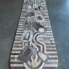 A long, oval wood sculpture with geometric lines sits atop a luxury designer rug.