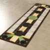 Luxury designer rug with geometric patterns in green, black, yellow, and beige on concrete.