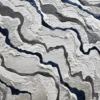 Close-up of a luxury designer rug with wavy, layered patterns in white, gray, and blue.