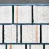 Luxury designer rug with handmade hide grid pattern in white, beige, and black bordered by blue lines on a gray floor.