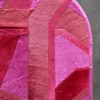 A close-up of the Vertigo Hide 15520 luxury designer rug with rounded corners and geometric pink and red pattern on a gray floor.