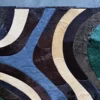 Drift Hide 29332 luxury designer rug with curved blue, brown, cream & green hide patches on a gray floor.