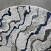 Close-up of designer luxury rug Submerge Hide 27443 with sculpted, textured waves in white, gray, and blue on a rounded high-end hide surface.