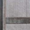 Close-up of a luxury custom designer wool rug, beige with dark stripe and border, on a dark floor.