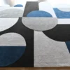 This luxury designer wool rug showcases abstract geometric circles and rectangles in black, white, gray, and blue.