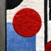 Luxury designer rug with geometric pattern, textured hide, and bold red accent on concrete.