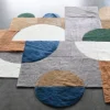 Luxury designer rug with geometric circles and rectangles in blue, brown, green, white, and gray on a gray floor.