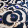 A close-up of Bloom Hide 15106 luxury designer rug shows textured, layered abstract patterns in black, beige, cream, brown, and blue.