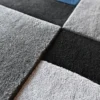 Close-up of Forms Wool 15486, a luxury designer rug with textured gray, black, and blue geometric squares.