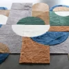 Forms Hide 29800 is a luxury designer rug featuring handmade hide pieces in geometric blue, green, tan, and brown shapes on a gray floor.
