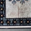 Close-up of the Winterlude Hide 26667 luxury designer rug with textured fur, black-gray geometric designs, and tan round details on a gray floor.